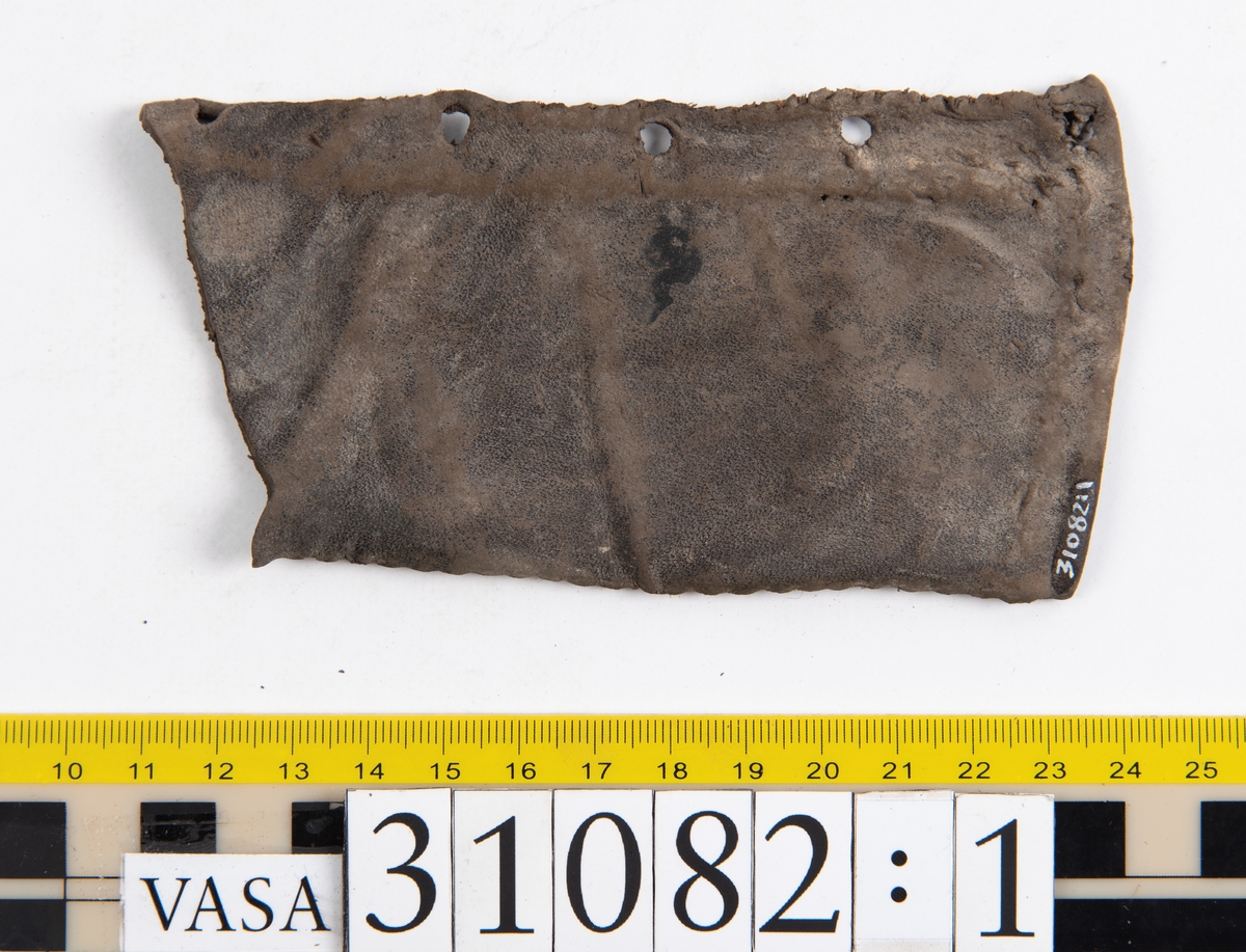 Dokumentation 1997:
Sju ospecificerade delar, troligtvis från klädedräkt.
Fyndnummer 31082 utgörs av ett rektangulärt läderstycke. Ena kortsidan är försedd med snörhål. Den nedre kanten är avklippt eller skuren samt försedd med ett kilformat jack. Den övre kanten är invikt och försedd med stygnshål. Längs med den andra kortsidan löper stygnshål.
Fyndnummer 31082:1 utgörs av ett rektangulärt läderstycke. Ena långsidan är försedd med snörhål och innanför snörhålen löper en stygnsrad. Längs med den andra långsidan löper stygnshål. Den ena kortsidan är invikt medan den motsatta kortsidan är avklippt eller skuren. Längs med den invikta kortsidan  löper stygnshål.
Fyndnummer 31082:2 utgörs av ett långsmalt läderstycke. Den ena kortsidan är försedd med två snörhål. Snörhålen fortsätter ner längs med ena långsidan. Innanför raden av snörhål löper stygnshål. Den motsatta långsidan är invikt. Den nedre kanten är avklippt eller skuren.
Fyndnummer 31082:3 utgörs av ett långsmalt läderstycke. Den ena långsidan är invikt och längs med den motsatta långsidan löper stygnshål. Längs med läderstyckets mitt löper snörhål. Den nedre kanten är avklippt eller skuren.
Fyndnummer 31082:4 utgörs av ett rektangulärt läderstycke. I läderstyckets ena hörn finns ett runt hål. Längs med långsidorna löper stygnshål. kortsidorna är avklippta eller skurna.
Fyndnummer 31082:5 består av två delar vars stygnshål går att passar ihop. Den ena delen består av ett långsmalt läderstycke. Längs med ena kortsidan löper stygnshål. Den andra delen består av ett rektangulärt läderstycke. Längs med ena långsidan löper stygnshål.

Dokumentation 2022:
31082:6 är ett stövelben till en stövel av polsk typ. Tillverkat i marockanskt getskinnläder. Inga dekorationer. Består av fem fragment som har blivit avskurna från skobotten, troligen för att återanvända lädret. Stövelbenet är delaminerat och vissa delar saknas.
För mer information, se Länkade filer: Uppritning

Text in english:
31082:6 is a bootleg from a Polish-style boot, made of Morocco goatskin leather, with no decorative features. The bootleg consists of five fragments that have been cut off from the bottom of the boot to salvage the leather. The bootleg has suffered from delamination and some parts are missing.
For more information, go to Länkade filer: Uppritning