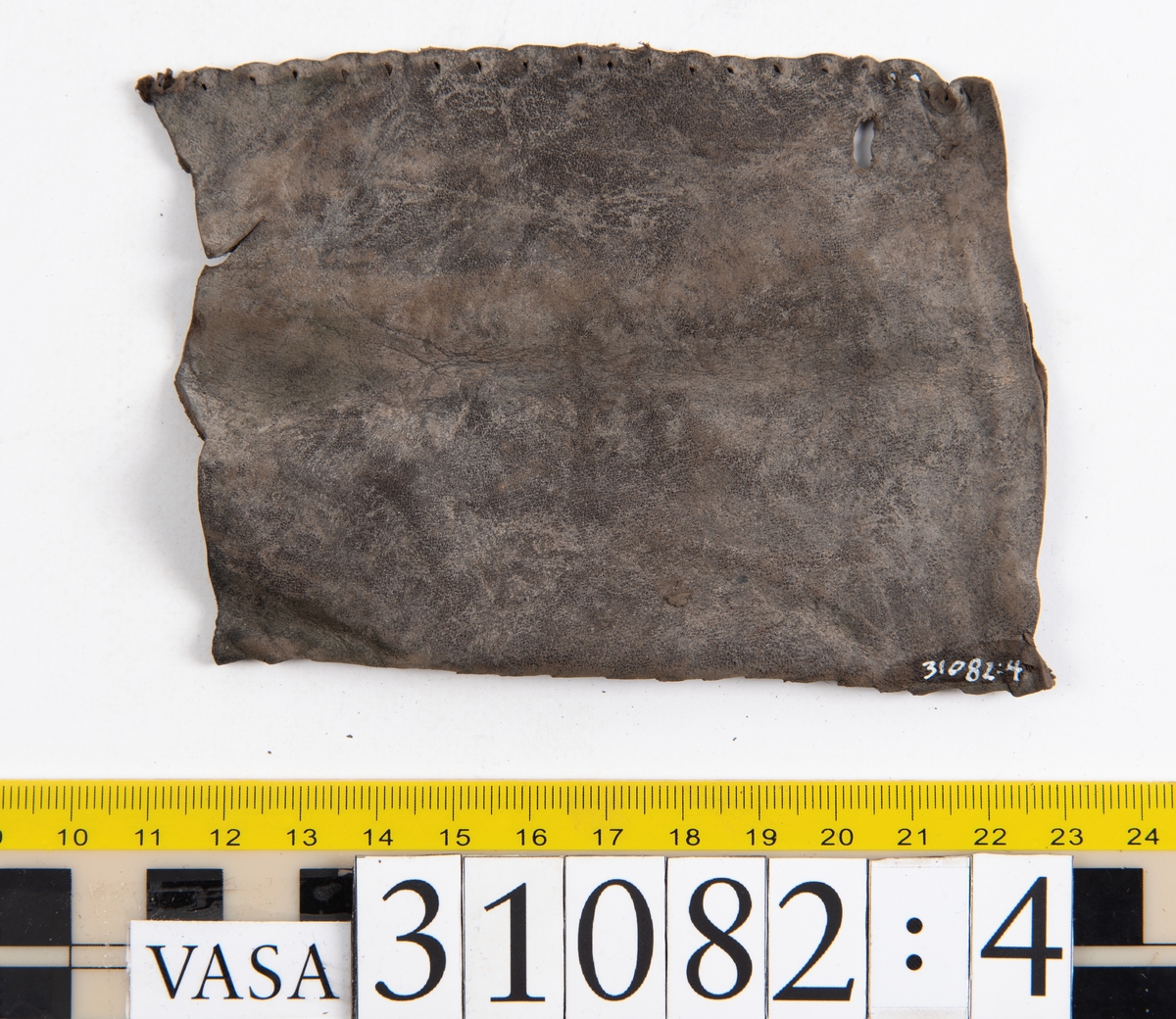 Dokumentation 1997:
Sju ospecificerade delar, troligtvis från klädedräkt.
Fyndnummer 31082 utgörs av ett rektangulärt läderstycke. Ena kortsidan är försedd med snörhål. Den nedre kanten är avklippt eller skuren samt försedd med ett kilformat jack. Den övre kanten är invikt och försedd med stygnshål. Längs med den andra kortsidan löper stygnshål.
Fyndnummer 31082:1 utgörs av ett rektangulärt läderstycke. Ena långsidan är försedd med snörhål och innanför snörhålen löper en stygnsrad. Längs med den andra långsidan löper stygnshål. Den ena kortsidan är invikt medan den motsatta kortsidan är avklippt eller skuren. Längs med den invikta kortsidan  löper stygnshål.
Fyndnummer 31082:2 utgörs av ett långsmalt läderstycke. Den ena kortsidan är försedd med två snörhål. Snörhålen fortsätter ner längs med ena långsidan. Innanför raden av snörhål löper stygnshål. Den motsatta långsidan är invikt. Den nedre kanten är avklippt eller skuren.
Fyndnummer 31082:3 utgörs av ett långsmalt läderstycke. Den ena långsidan är invikt och längs med den motsatta långsidan löper stygnshål. Längs med läderstyckets mitt löper snörhål. Den nedre kanten är avklippt eller skuren.
Fyndnummer 31082:4 utgörs av ett rektangulärt läderstycke. I läderstyckets ena hörn finns ett runt hål. Längs med långsidorna löper stygnshål. kortsidorna är avklippta eller skurna.
Fyndnummer 31082:5 består av två delar vars stygnshål går att passar ihop. Den ena delen består av ett långsmalt läderstycke. Längs med ena kortsidan löper stygnshål. Den andra delen består av ett rektangulärt läderstycke. Längs med ena långsidan löper stygnshål.

Dokumentation 2022:
31082:6 är ett stövelben till en stövel av polsk typ. Tillverkat i marockanskt getskinnläder. Inga dekorationer. Består av fem fragment som har blivit avskurna från skobotten, troligen för att återanvända lädret. Stövelbenet är delaminerat och vissa delar saknas.
För mer information, se Länkade filer: Uppritning

Text in english:
31082:6 is a bootleg from a Polish-style boot, made of Morocco goatskin leather, with no decorative features. The bootleg consists of five fragments that have been cut off from the bottom of the boot to salvage the leather. The bootleg has suffered from delamination and some parts are missing.
For more information, go to Länkade filer: Uppritning
