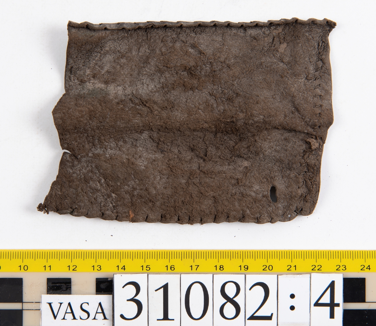Dokumentation 1997:
Sju ospecificerade delar, troligtvis från klädedräkt.
Fyndnummer 31082 utgörs av ett rektangulärt läderstycke. Ena kortsidan är försedd med snörhål. Den nedre kanten är avklippt eller skuren samt försedd med ett kilformat jack. Den övre kanten är invikt och försedd med stygnshål. Längs med den andra kortsidan löper stygnshål.
Fyndnummer 31082:1 utgörs av ett rektangulärt läderstycke. Ena långsidan är försedd med snörhål och innanför snörhålen löper en stygnsrad. Längs med den andra långsidan löper stygnshål. Den ena kortsidan är invikt medan den motsatta kortsidan är avklippt eller skuren. Längs med den invikta kortsidan  löper stygnshål.
Fyndnummer 31082:2 utgörs av ett långsmalt läderstycke. Den ena kortsidan är försedd med två snörhål. Snörhålen fortsätter ner längs med ena långsidan. Innanför raden av snörhål löper stygnshål. Den motsatta långsidan är invikt. Den nedre kanten är avklippt eller skuren.
Fyndnummer 31082:3 utgörs av ett långsmalt läderstycke. Den ena långsidan är invikt och längs med den motsatta långsidan löper stygnshål. Längs med läderstyckets mitt löper snörhål. Den nedre kanten är avklippt eller skuren.
Fyndnummer 31082:4 utgörs av ett rektangulärt läderstycke. I läderstyckets ena hörn finns ett runt hål. Längs med långsidorna löper stygnshål. kortsidorna är avklippta eller skurna.
Fyndnummer 31082:5 består av två delar vars stygnshål går att passar ihop. Den ena delen består av ett långsmalt läderstycke. Längs med ena kortsidan löper stygnshål. Den andra delen består av ett rektangulärt läderstycke. Längs med ena långsidan löper stygnshål.

Dokumentation 2022:
31082:6 är ett stövelben till en stövel av polsk typ. Tillverkat i marockanskt getskinnläder. Inga dekorationer. Består av fem fragment som har blivit avskurna från skobotten, troligen för att återanvända lädret. Stövelbenet är delaminerat och vissa delar saknas.
För mer information, se Länkade filer: Uppritning

Text in english:
31082:6 is a bootleg from a Polish-style boot, made of Morocco goatskin leather, with no decorative features. The bootleg consists of five fragments that have been cut off from the bottom of the boot to salvage the leather. The bootleg has suffered from delamination and some parts are missing.
For more information, go to Länkade filer: Uppritning