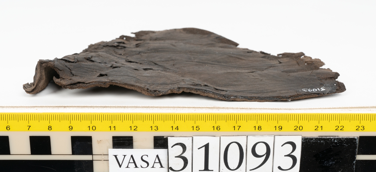 Ett ovanläder till en sko. Ovanlädrets övre kant är rakt avskuren och saknar tunga. Nedanför den övre kanten sitter två snörhål. Längs med ytterkanterna löper stygnshål. Ena ytterkanten är fragmentarisk.