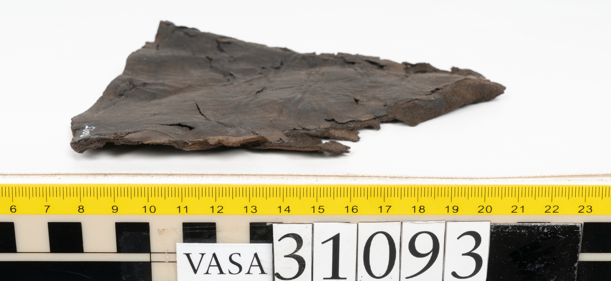 Ett ovanläder till en sko. Ovanlädrets övre kant är rakt avskuren och saknar tunga. Nedanför den övre kanten sitter två snörhål. Längs med ytterkanterna löper stygnshål. Ena ytterkanten är fragmentarisk.