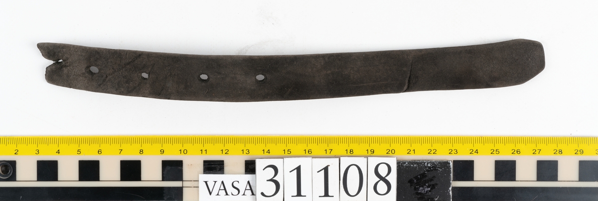 Två delar av en läderrem.
Den längsta delen av remmen är försedd med fem hål. Det femte hålet är placerat vid remmens fragmentariska ände. Den motsvarande änden är kantigt skuren. Lädret är mycket kraftigt och välbevarat.
Den kortare delen av remmen är försedd med en fragmentarisk ände samt en rakt skuren eller avklippt ände. Strax innanför den skurna änden finns ett större hål som är försett med fasade kanter. Narvsidan är så gott som helt bortspaltad, i övrigt är lädret kraftigt och relativt välbevarat.