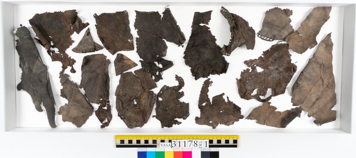 Runt 400 delar och fragment från skor i form av sulor, inlägg, ovanläder, klack, sidostycken, bakkappor, träpliggar, tråd mm. Troligtvis rör det sig om delar och fragment från flera skor och/eller stövlar. Delar av lädret har förstärkts med lim av konserveringsenheten. Merparten av lädret är spaltat samt har hål efter träpligg eller stygn.