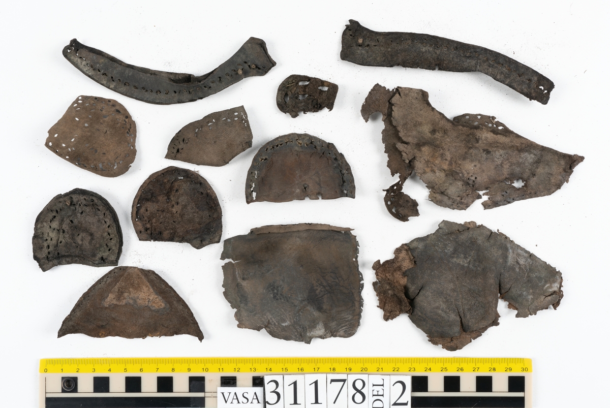 Runt 400 delar och fragment från skor i form av sulor, inlägg, ovanläder, klack, sidostycken, bakkappor, träpliggar, tråd mm. Troligtvis rör det sig om delar och fragment från flera skor och/eller stövlar. Delar av lädret har förstärkts med lim av konserveringsenheten. Merparten av lädret är spaltat samt har hål efter träpligg eller stygn.