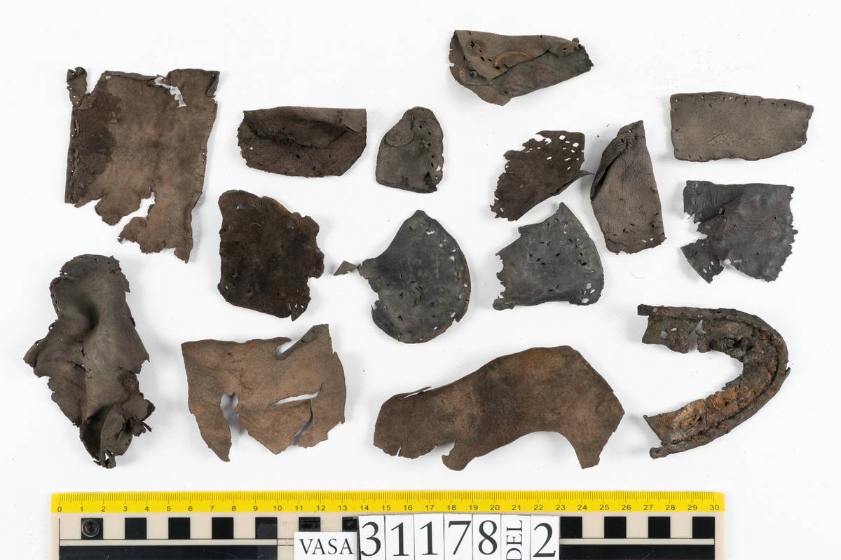 Runt 400 delar och fragment från skor i form av sulor, inlägg, ovanläder, klack, sidostycken, bakkappor, träpliggar, tråd mm. Troligtvis rör det sig om delar och fragment från flera skor och/eller stövlar. Delar av lädret har förstärkts med lim av konserveringsenheten. Merparten av lädret är spaltat samt har hål efter träpligg eller stygn.