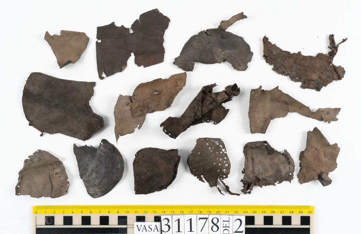 Runt 400 delar och fragment från skor i form av sulor, inlägg, ovanläder, klack, sidostycken, bakkappor, träpliggar, tråd mm. Troligtvis rör det sig om delar och fragment från flera skor och/eller stövlar. Delar av lädret har förstärkts med lim av konserveringsenheten. Merparten av lädret är spaltat samt har hål efter träpligg eller stygn.