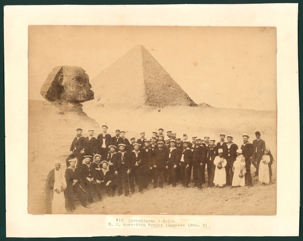 Bilden föreställer korvetten FREJAS besättning som har tagit uppställning framför sfinxen och pyramiderna för en gruppfoto under långresan 1889-90.