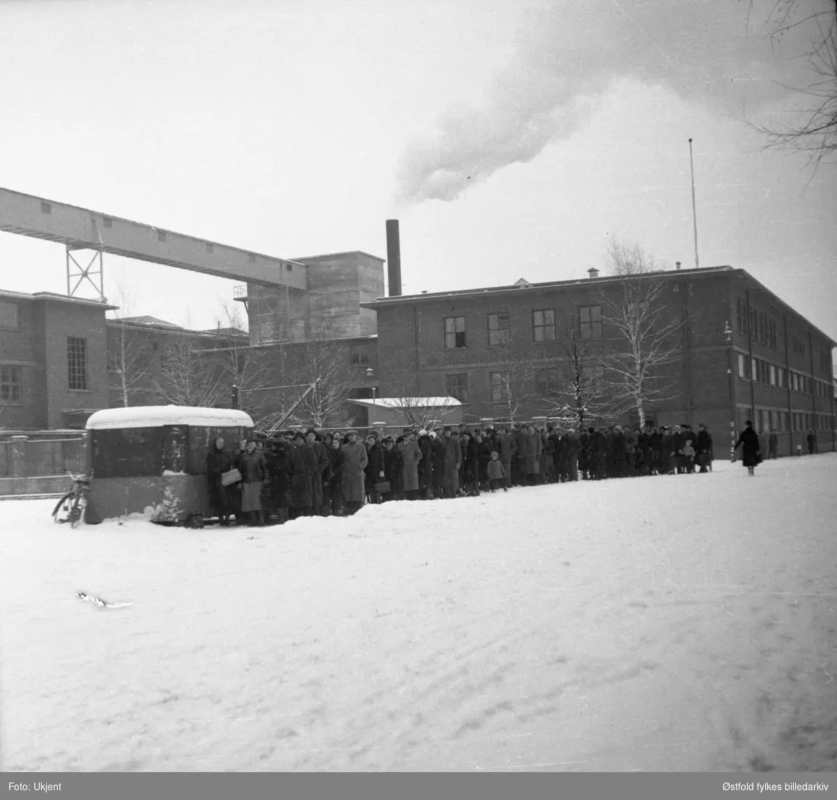 Folk i kø for kjøtt og fisk under 2. verdenskrig i Askim 1940-1945. I bakgrunnen Askim gummivarefabrikk.