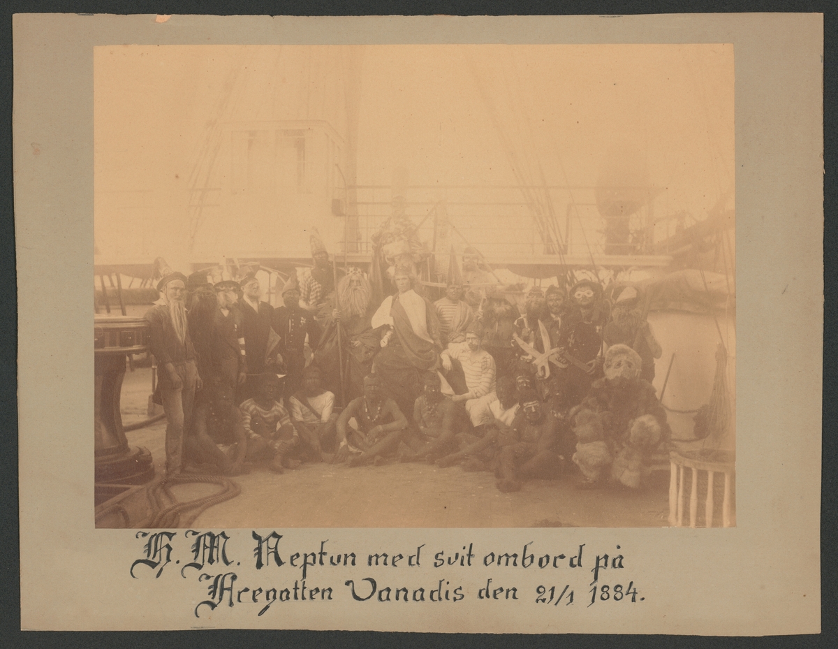 Bilden föreställer en grupp fantasifull utklädda sjömän som har samlats på däck inför neptunifesten vid passerandet av linjen 21/1 1884 ombord på fregatten Vanadis världsomsegling 1883-85.