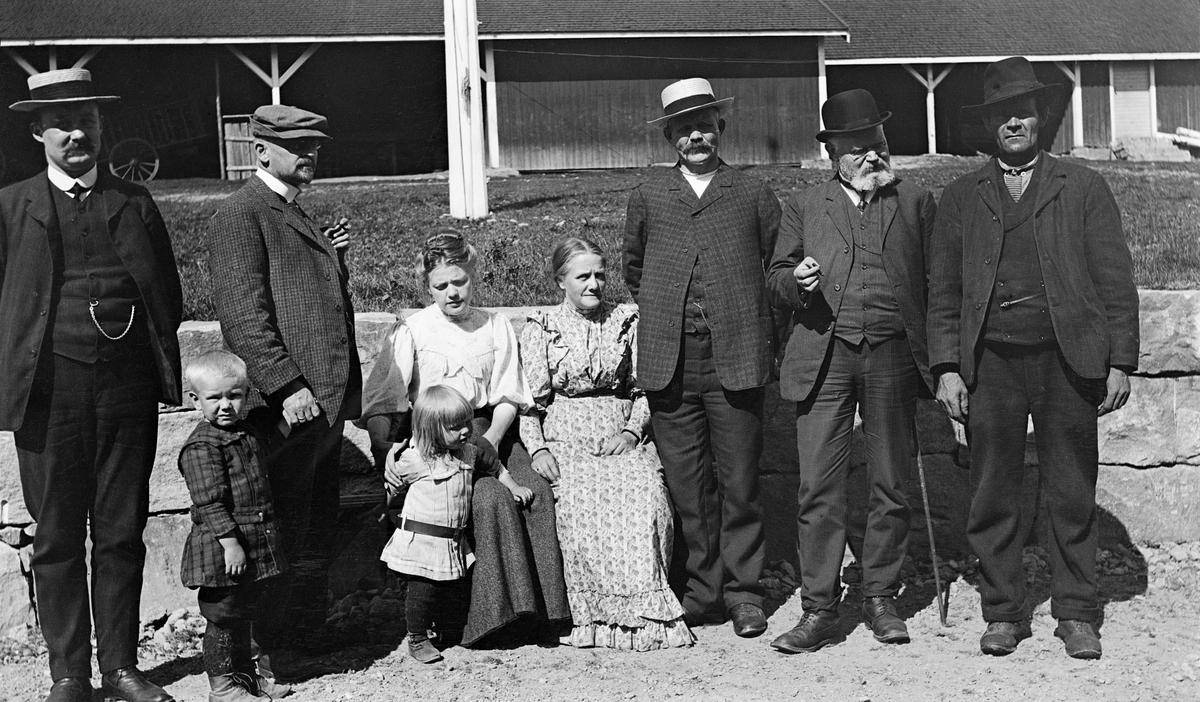 Gruppebilde, tatt i tunet på Gravbergsgarden i Våler i 1909. Til venstre ser vi skogsbestyrer Ole Larsen Kortgaard. Deretter følger barnebarnet Thor Emilsen Røsaas, svigersønnen Emil Pedersen Rørsaas, dattera Olea Røsaas, barnebarnet Margot Emilsdatter Røsaas og kona Torine Kortgaard. De to neste mennene i rekka er antakelig medlemmer av styret i Christiania Tømmerdirektion, som var på befaring i Gravberget da dette fotografiet. Mannen nest ytterst er disponent Bernhard Magnus Kopperud. Mannen ytterst til høyre kan ha vært en av dem som bodde og arbeidet i Gravbergsgarden, som var administrasjonssenter for Borregaards skoger i denne regionen.