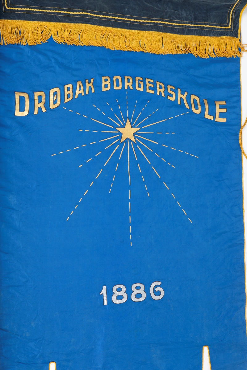 Skolefane for Drøbak borgerskole/Drøbak høiere almenskole. Fanen laget til skolen 50-års jubileum i 1936. Silke eller kunstsilke. 
Ene siden rødt stoff med malt skrift og dekorasjon i sølv og gull: 
"DRØBAK HØIERE ALMENSKOLE   Å TENKE FRITT ER STORT   Å TENKE RETT ER STØRRE"
"1886 23 august. 1936 23. august"

Den andre siden blått stoff med malt dekorasjon i gull: Stjerne med stråler "DRØBAK BORGERSKOLE" 
En mørk blå fløyelskant dekker fanen helt øverst. Denne kan være sekundær. 
Fanen er utstyrt med gullsnorer og dusker. Fanen er festet til en trestang med store metallkuler i endene. Trestangen kan være sekundær da det ser ut til at metallkulene har vært festet annerledes. 
Mye tyder på at fanen har vært hengt opp da det er kroker festet til stangen.

Påskrift: Drøbak Borgerskole 1886.
             Drøbak høiere allmennskole
             Å tenke fritt er stort
             Å tenke rett er større