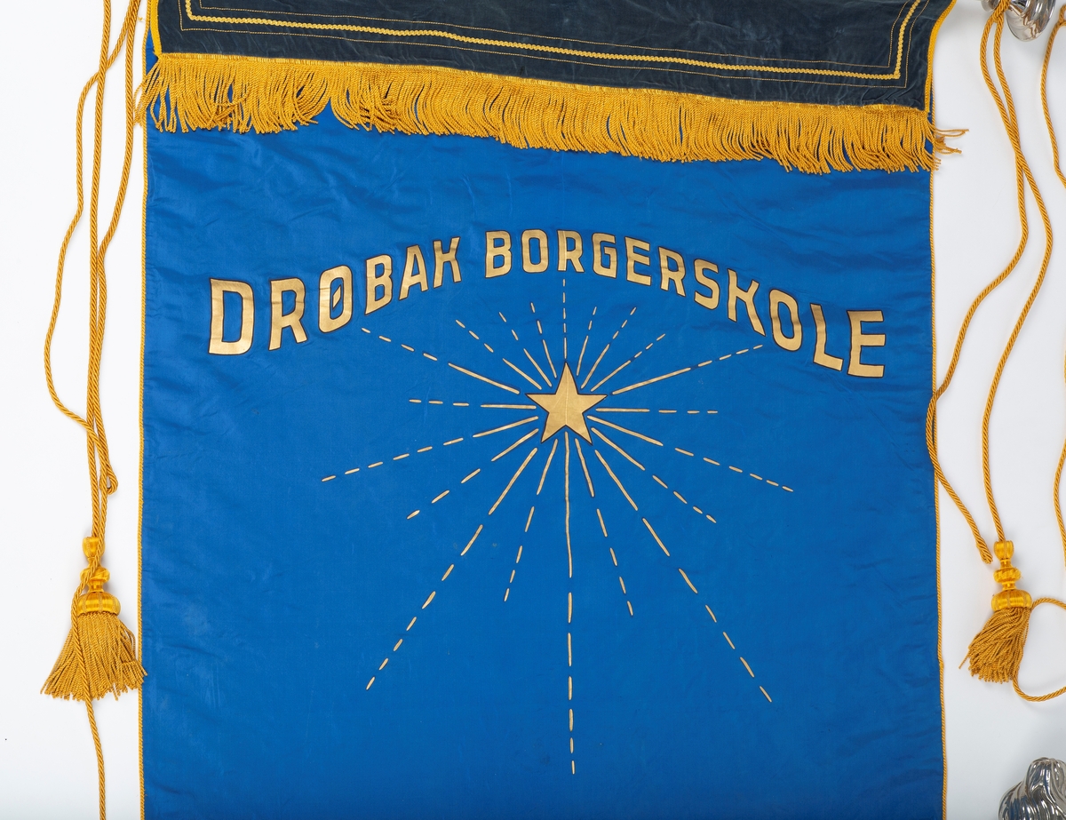 Skolefane for Drøbak borgerskole/Drøbak høiere almenskole. Fanen laget til skolen 50-års jubileum i 1936. Silke eller kunstsilke. 
Ene siden rødt stoff med malt skrift og dekorasjon i sølv og gull: 
"DRØBAK HØIERE ALMENSKOLE   Å TENKE FRITT ER STORT   Å TENKE RETT ER STØRRE"
"1886 23 august. 1936 23. august"

Den andre siden blått stoff med malt dekorasjon i gull: Stjerne med stråler "DRØBAK BORGERSKOLE" 
En mørk blå fløyelskant dekker fanen helt øverst. Denne kan være sekundær. 
Fanen er utstyrt med gullsnorer og dusker. Fanen er festet til en trestang med store metallkuler i endene. Trestangen kan være sekundær da det ser ut til at metallkulene har vært festet annerledes. 
Mye tyder på at fanen har vært hengt opp da det er kroker festet til stangen.

Påskrift: Drøbak Borgerskole 1886.
             Drøbak høiere allmennskole
             Å tenke fritt er stort
             Å tenke rett er større