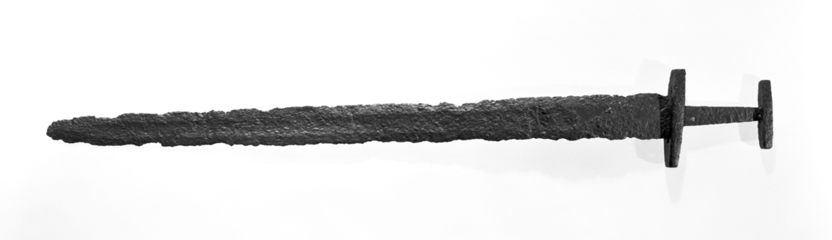 Sverd av jern som Petersen: Vikingesverd fig. 98, type M. Det er ganske velbevart, men det har nok flaknet av en del rust. 84,3 cm langt. Sverdet hang no på sorenskriverkontoret på Skei, Førde s og p, Sogn og Fjordane. Ifølge en vedhengt lapp er det funnet på loftet i hovedbygningen i 1924, og det lyktes den gang ikke å få rede på hvor det var kommet fra. Lappen er signert av daværende sorenskriver. Sannsynligvis er det funnet på sorenskrivergården, gnr. 21 bnr. 24. Innbrakt av Fett
Revisjon 2019: Tveegget sverd, Petersens type M. Klingen har mindre hakk langs eggen, og odden er skadet. Klingen er svakt bøyd. 