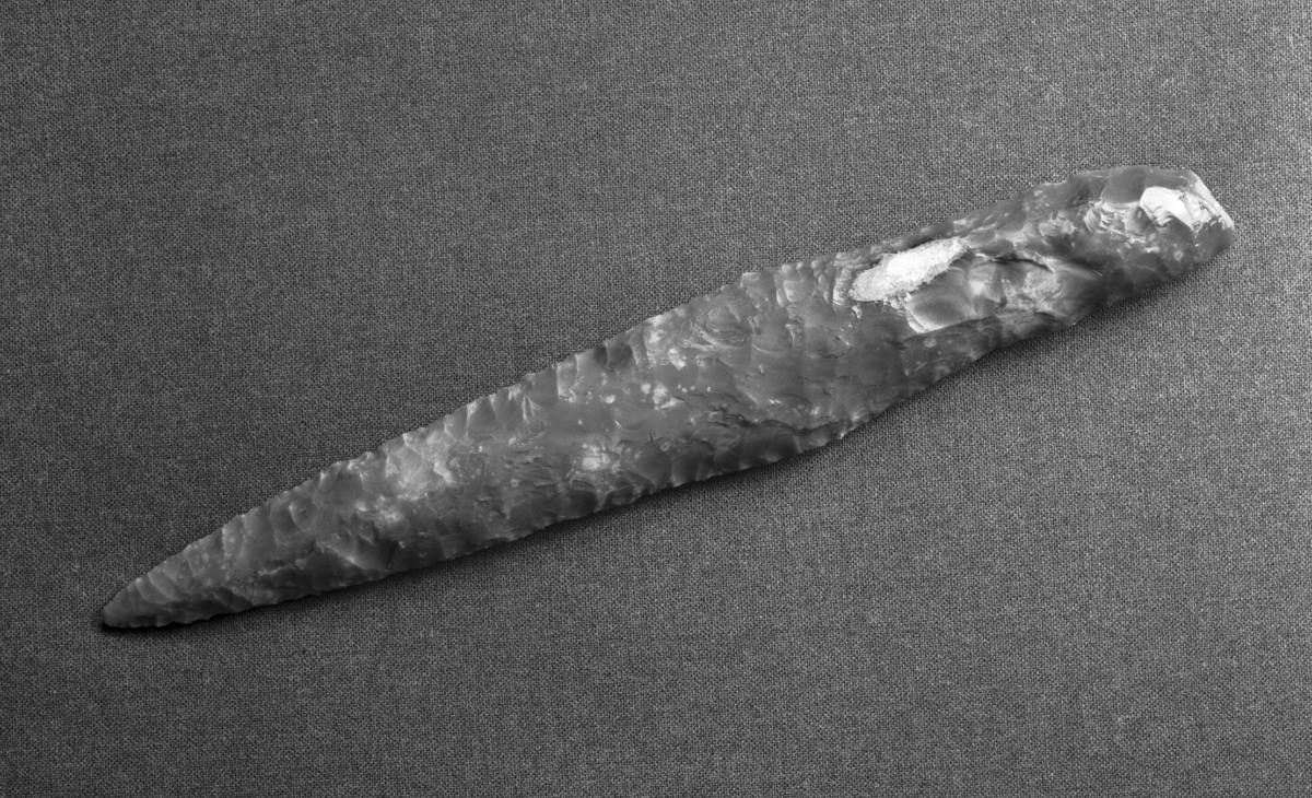 Flintdolk, meget vel bevart, som R 71 hos Rygh 1885, men mindre markerte skuldre. Sømmene langs siden av håndtaket er avknuste og tydelig slitt. L. 24,5 cm, derav bladet 16 cm, bladets st. br. ved roten 3,7 cm. Funnet på Ålesund gravsted, Ålesund, Møre og Romsdal, for 15 -20 år siden. Gave fra Karsten Remvik, Sørnesvegen 20, 6000 Ålesund