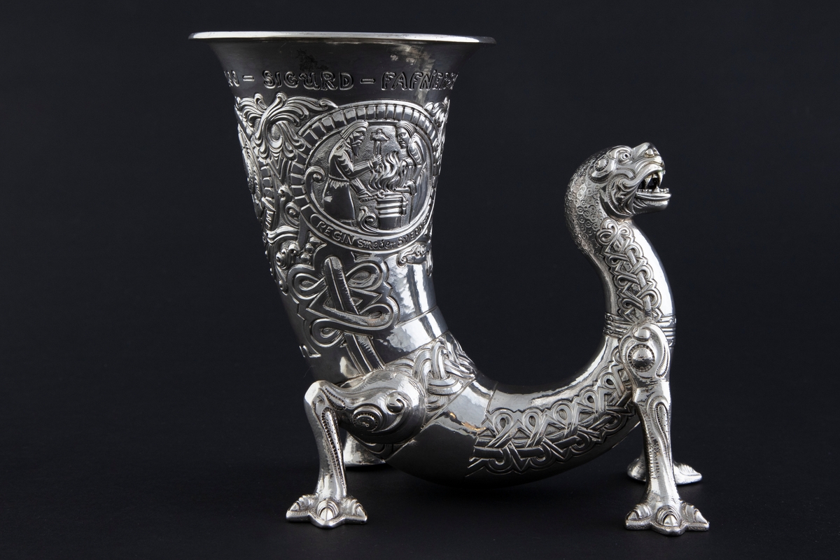 På øvre del av drikkehornet er det tre sirkulære felter med motiver fra historien om Sigurd Favnesbane, hentet fra Hyllestadportalen. De er omgitt av ranker og flettverkornamentikk. De tre scenene er flankert av innskrifter. Figurene er sterkt stiliserte.

1) "REGIN smeder SVERDET". Scenen viser Regin og Sigurd som smir sverdet på en ambolt, med flammende ild i bakgrunnen. 

2) "SIGURD pröver SVERDET". Scenen viser Sigurd som slår sverdet mot armbolten, og det brekker i to. Regin står sentralt i feltet og betrakter hendelsen.

3) "SIGURD dreper DRAGEN". Scenen viser Sigurd som dreper den buktende dragen Favne. Den er bygget opp gjennom en horror vacui-prinsipp, hvor figurene fyller hele billedfeltet.