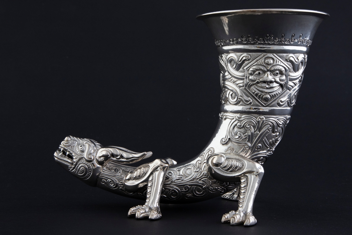 Drikkehorn i sølv som hviler på fire føtter med klør. Enden av hornet er utformet som et dragehode, mens øvre del er dekorert med to middelalderske masker; den ene smiler, mens den andre har et sint uttrykk. Yttersiden er dekorert med flettverksornamentikk, som trolig opprinnelig har vært oksidert for å forsterke kontrasten til de blanke partiene. Innsiden har rester av forgylling.