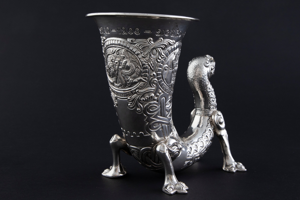 På øvre del av drikkehornet er det tre sirkulære felter med motiver fra historien om Sigurd Favnesbane, hentet fra Hyllestadportalen. De er omgitt av ranker og flettverkornamentikk. De tre scenene er flankert av innskrifter. Figurene er sterkt stiliserte.

1) "REGIN smeder SVERDET". Scenen viser Regin og Sigurd som smir sverdet på en ambolt, med flammende ild i bakgrunnen. 

2) "SIGURD pröver SVERDET". Scenen viser Sigurd som slår sverdet mot armbolten, og det brekker i to. Regin står sentralt i feltet og betrakter hendelsen.

3) "SIGURD dreper DRAGEN". Scenen viser Sigurd som dreper den buktende dragen Favne. Den er bygget opp gjennom en horror vacui-prinsipp, hvor figurene fyller hele billedfeltet.