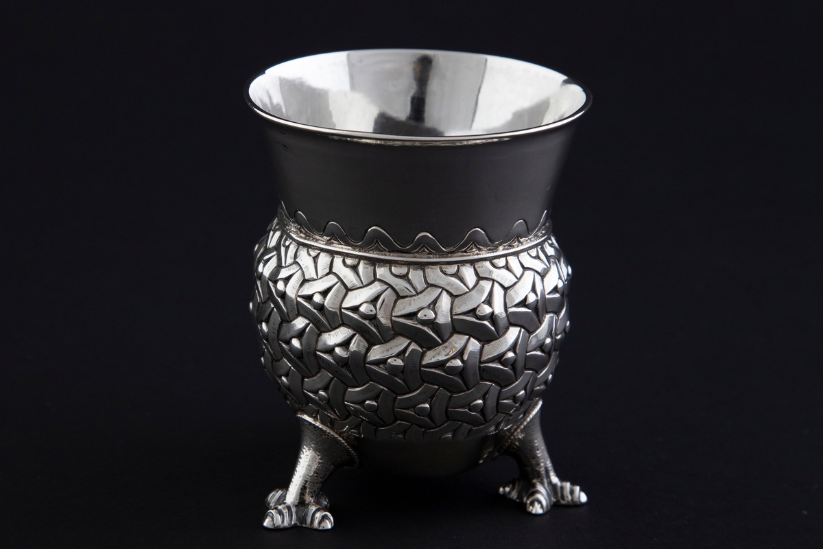 Sølvbeger. Kuleformet korpus hvis ytterside er dekorert med "entrelacs" (sammenkjedete trekanter med konkave sider). Det bæres av tre støpte drageben. Øvre del av begeret er konisk med bølgeformet dekor nederst.