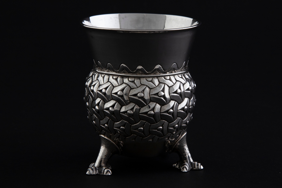 Sølvbeger. Kuleformet korpus hvis ytterside er dekorert med "entrelacs" (sammenkjedete trekanter med konkave sider). Det bæres av tre støpte drageben. Øvre del av begeret er konisk med bølgeformet dekor nederst.