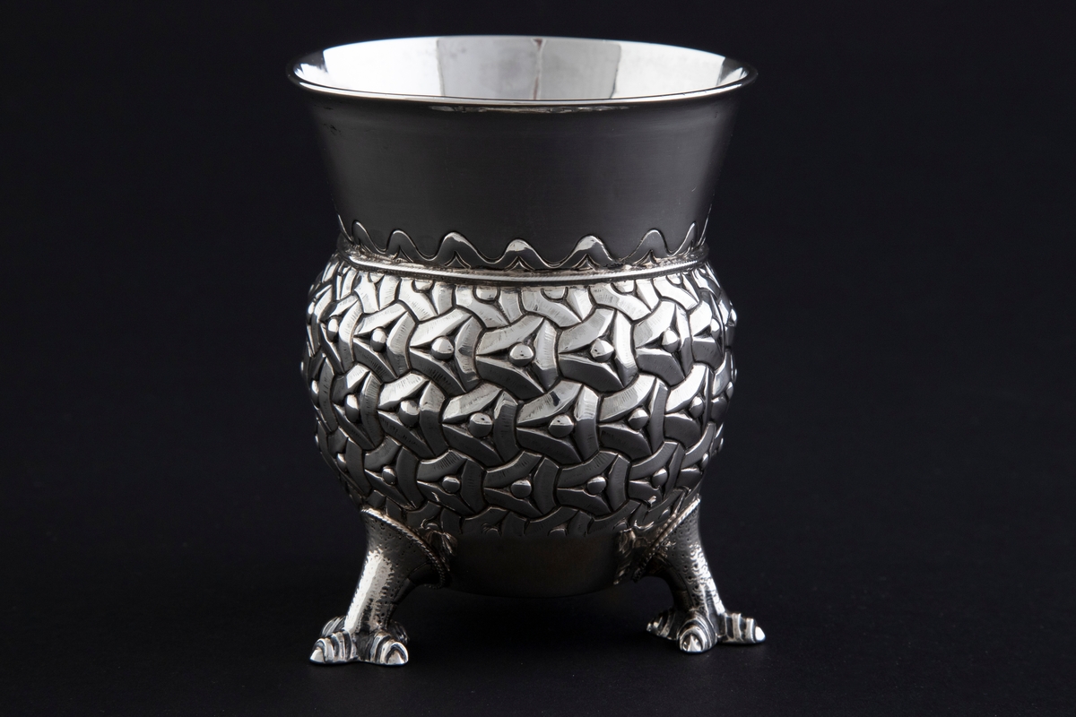 Sølvbeger. Kuleformet korpus hvis ytterside er dekorert med "entrelacs" (sammenkjedete trekanter med konkave sider). Det bæres av tre støpte drageben. Øvre del av begeret er konisk med bølgeformet dekor nederst.