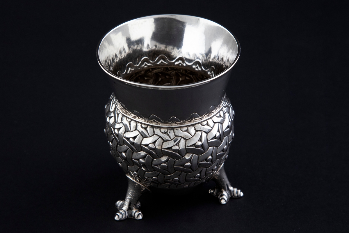 Sølvbeger. Kuleformet korpus hvis ytterside er dekorert med "entrelacs" (sammenkjedete trekanter med konkave sider). Det bæres av tre støpte drageben. Øvre del av begeret er konisk med bølgeformet dekor nederst.