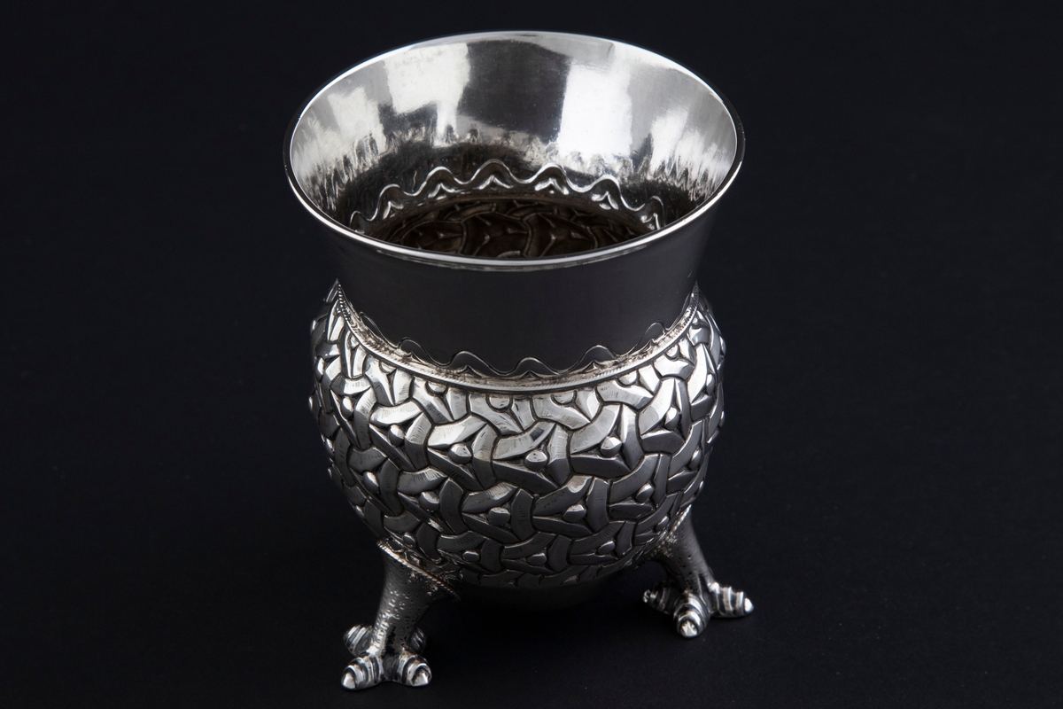 Sølvbeger. Kuleformet korpus hvis ytterside er dekorert med "entrelacs" (sammenkjedete trekanter med konkave sider). Det bæres av tre støpte drageben. Øvre del av begeret er konisk med bølgeformet dekor nederst.