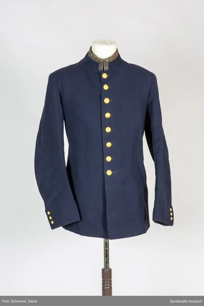 Enkelknäppt polisuniform med ståndkrage med broderade liggande eklöv. Förgyllda knappar med länsvapnet..
