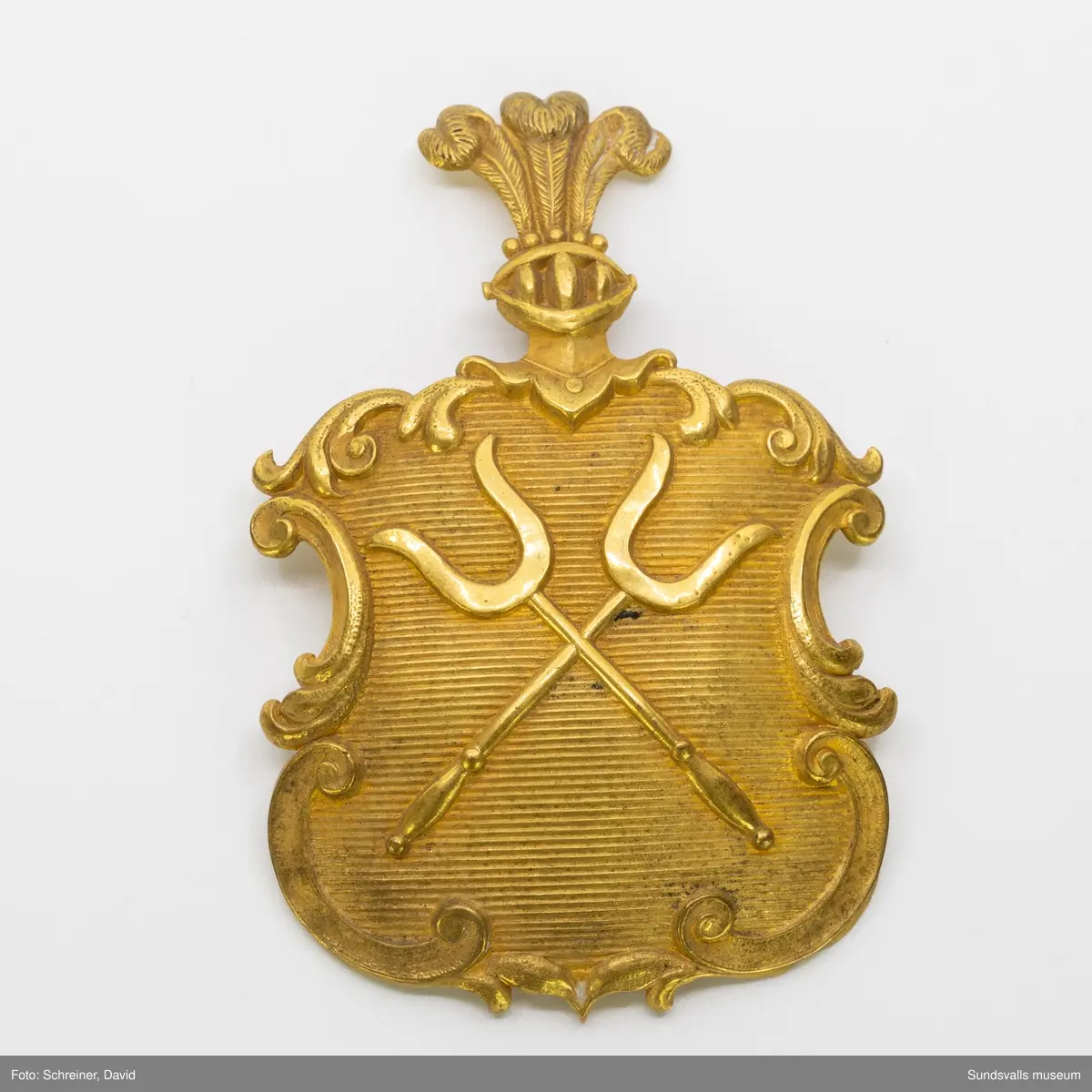 Präglat emblem för kask med två korslagda muskötgafflar.