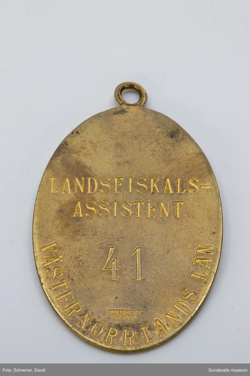 På framsidan med riksvapnet i skölden och bakom eklövskrans runt skölden
