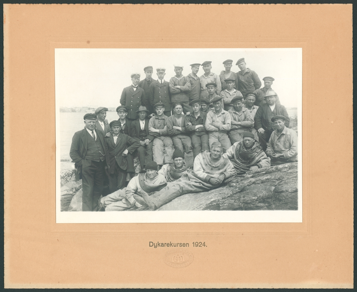 Denna grupporträtt föreställer dykarekursen 1924. En grupp marinkårssoldater har tagit plats på en klippa. I första raden ligger fyra män som bär tungdykardräkt. I andra raden är det arbetskläder som gäller och högst upp bär man sjömanskostym.