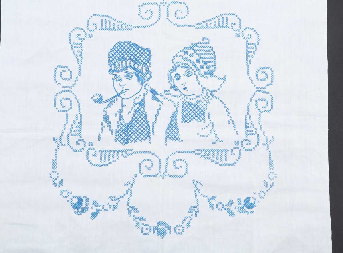 Pyntehåndkle, Hvit bunn, blå kanter. Brodert med en gutt og ei jente med korsting. Monogram M.

Gitt av Erna Madsen. Produsert av Margit Madsen.
Disse drev manufaktur i Drøbak.