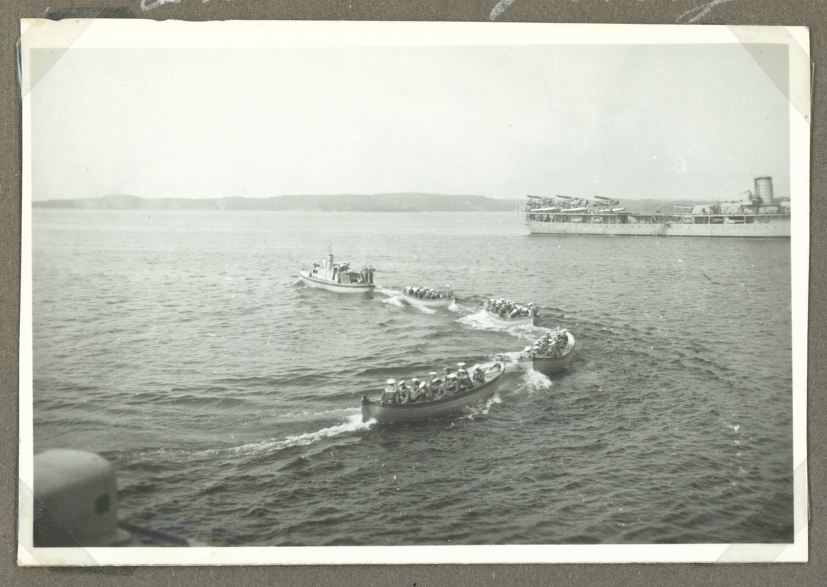 Bilden visar fyra roddbåtar som är fullsatta med sjömän som bogseras av en ångbarkass.