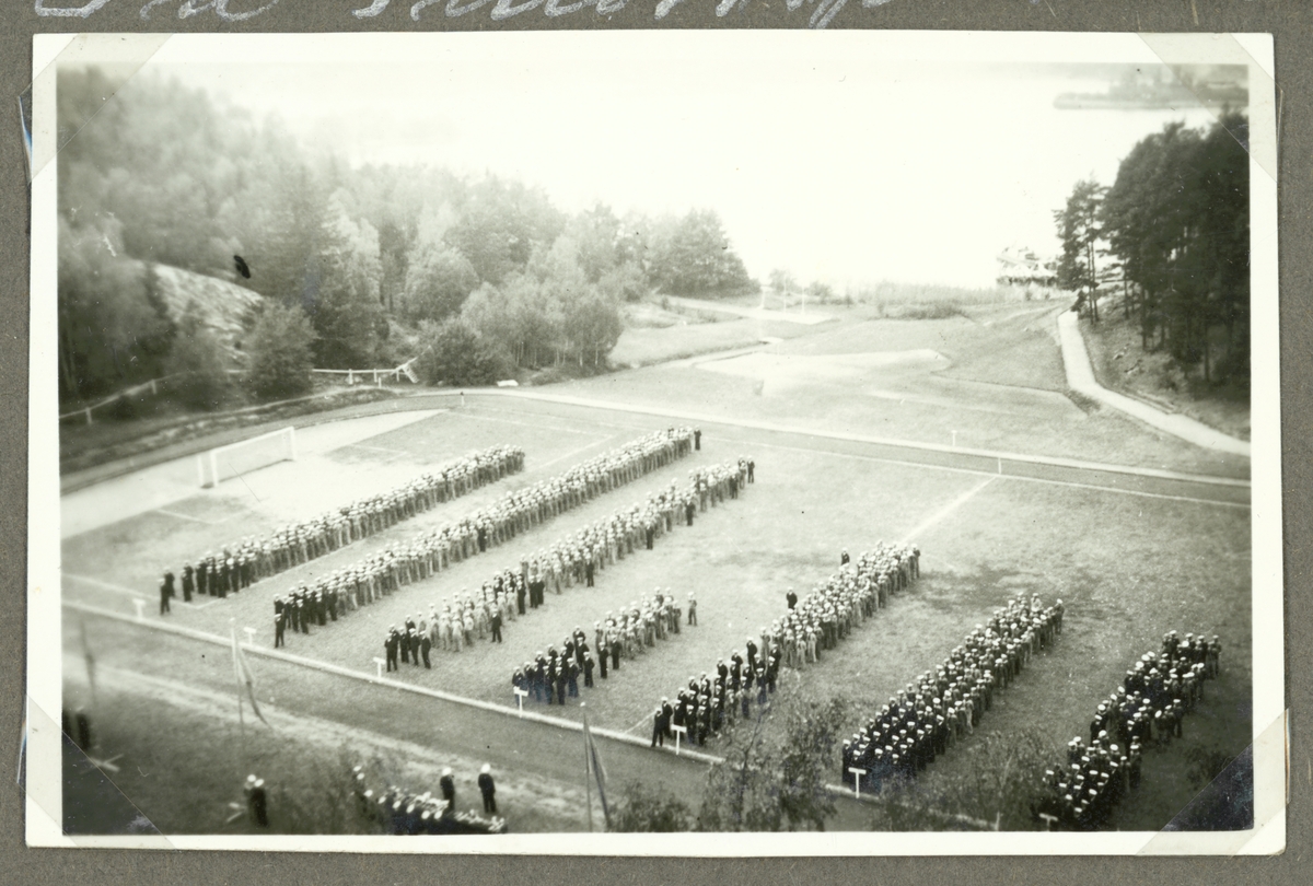 Bilden visar uppställning av militärer på en idrottsplats.
