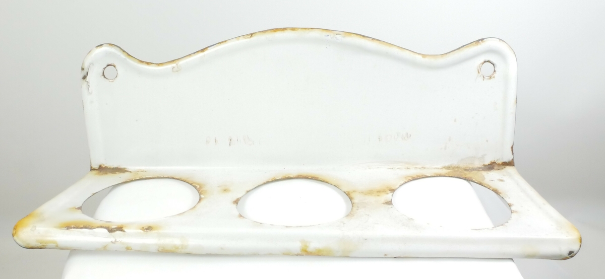 Hylle i metall. Bølgete kant med to hull i hvert hjørne til å feste på vegg. Nederst er det tre hull til feste av beholdere. 3 runde beholdere med blå kant tilhører hyllen. 