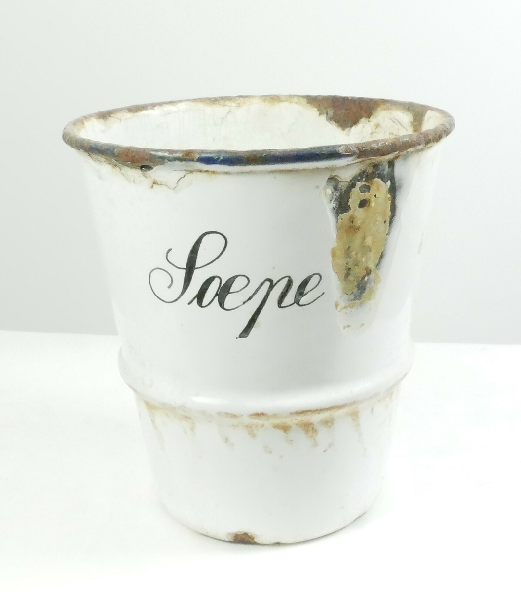 Hylle i metall. Bølgete kant med to hull i hvert hjørne til å feste på vegg. Nederst er det tre hull til feste av beholdere. 3 runde beholdere med blå kant tilhører hyllen. 