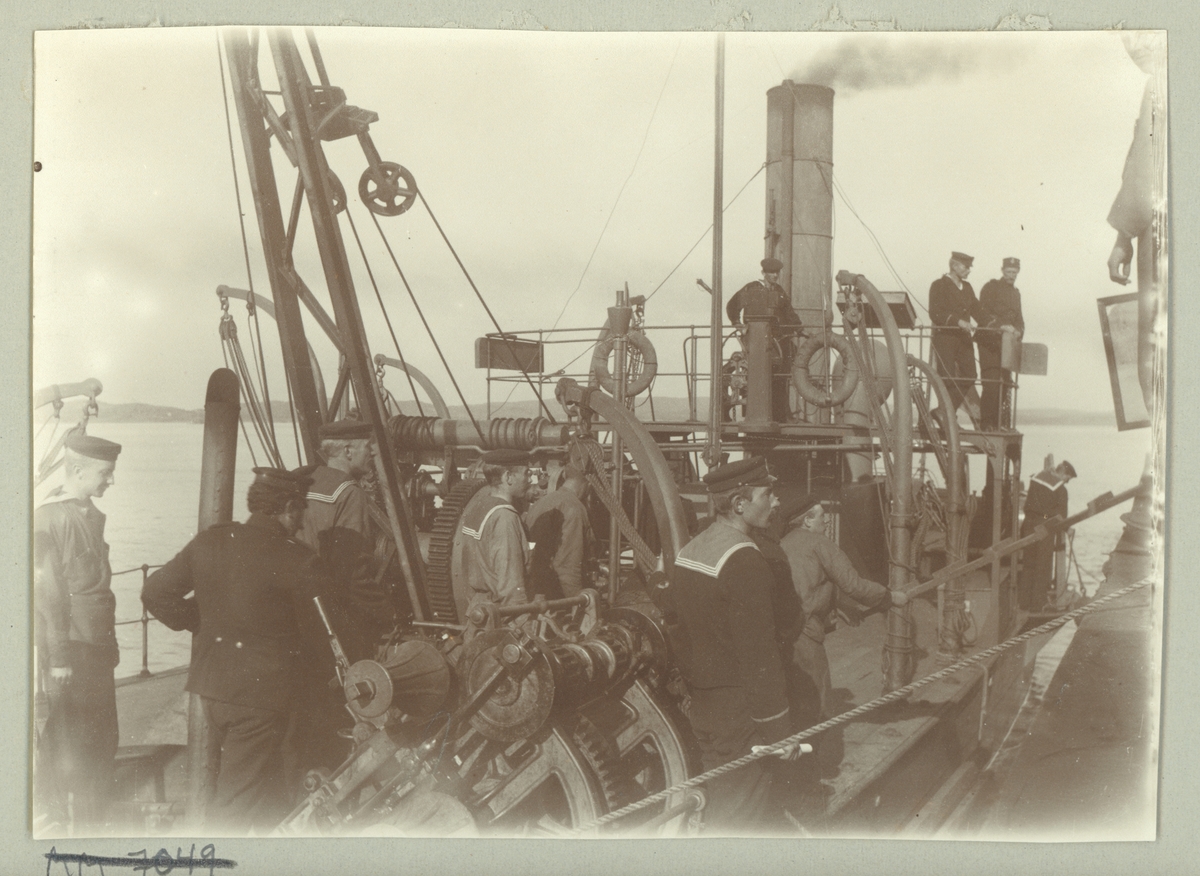 Bilden visar sjömän ombord på ångkranpråm nr 8. Pråmen har precist förtöjt vid kajen och männen håller på att lägga över landgången.