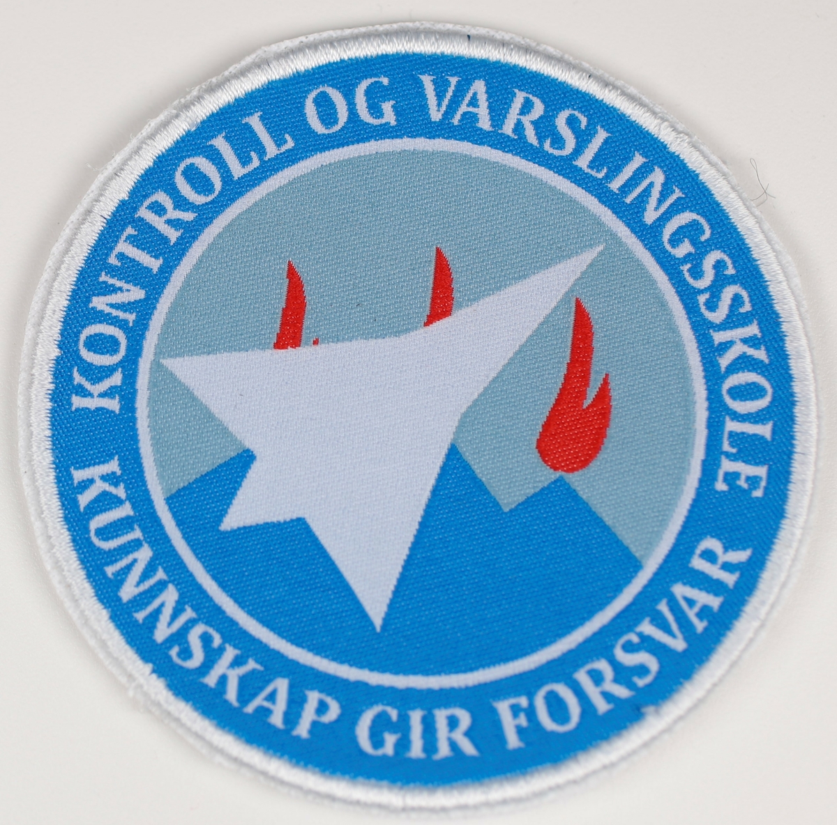 Varder med røde flammer på blå bakgrunn, omriss av sølvfarget fly i forgrunn.