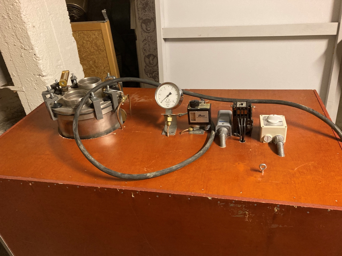 Stort hjemmebrentsapparat. Tanken er innebygd i en kasse av kryssfinér og hengslett lokk. På instrumentene som hører med står det: Bergs Maskin, Trondheim kp/cm2, Ranco, Trade mark registered, Penn. En stor sikring og en bryter 0-1-2.