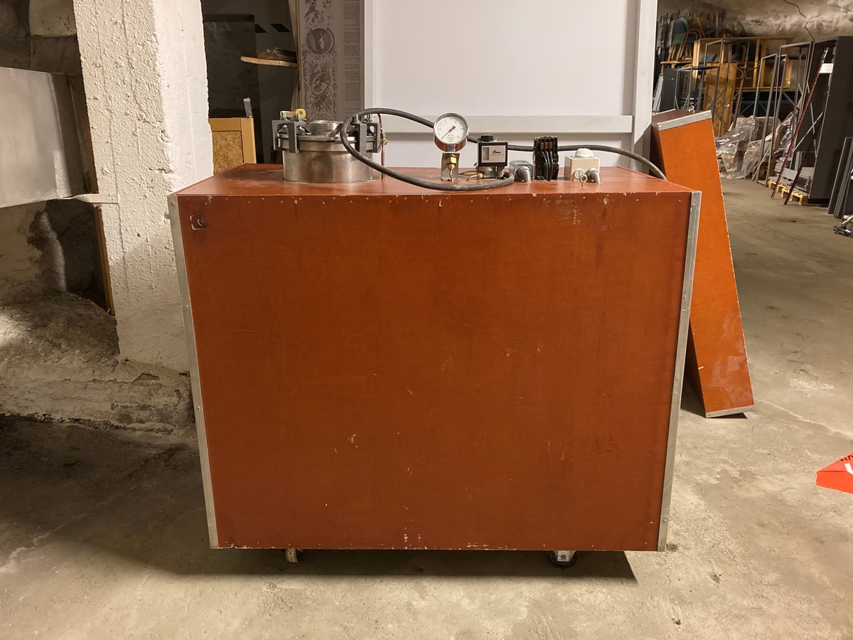 Stort hjemmebrentsapparat. Tanken er innebygd i en kasse av kryssfinér og hengslett lokk. På instrumentene som hører med står det: Bergs Maskin, Trondheim kp/cm2, Ranco, Trade mark registered, Penn. En stor sikring og en bryter 0-1-2.