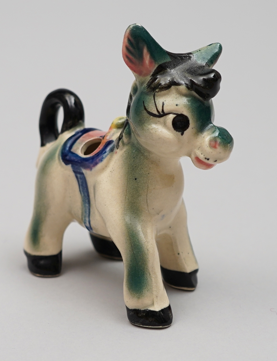 Eselfigur i steingods, måla dekor. Eit hol på kvar side av sadelen.