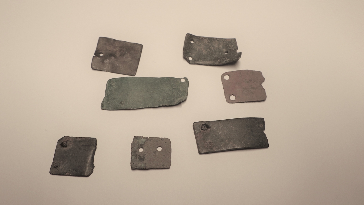 MALV: 15*13 - 26*17 MM, REKTANGULÆR BÅNDFORMET MED TO HULL I ENE ENDEN, AVBRUKKET I ANDRE. TO FRAGMENTER HAR ISITTENDE NAGLER OG ETT FRAGMENTHAR BARE ET HULL I ENDEN. 