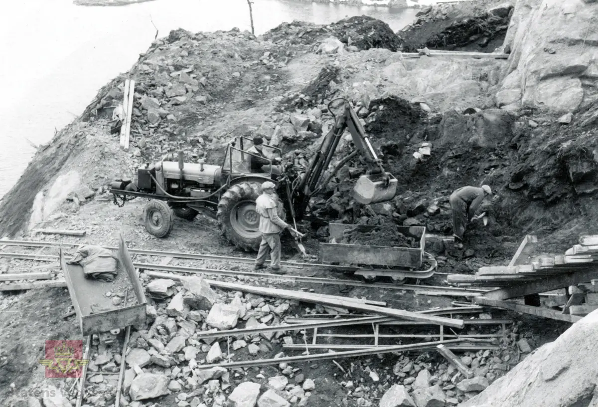 Fra bygging av Tromøybrua som ble åpnet 21. oktober 1961. 
Fordson Major traktor med påmontert graveaggregat (traktorgraver). Vagge med masse transporteres på skinnegangen.

Vegbru. Hengebru med fagverk, ingen opphengte sidespenn. Lengde 400, 30 meter. Spenn antall/største 12 / 240,00 meter.
Kilde: Statens vegvesen sitt bruregister  " Brutus" nr. 09-0406 Tromøybrua.

Stedsnavn: Tromøy