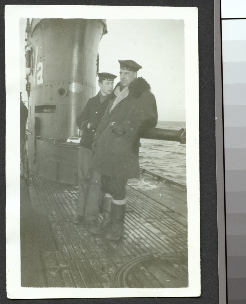 Bilden föreställer två sjömån som står på däck av ubåten Valen och lutar sig mot kanonen.