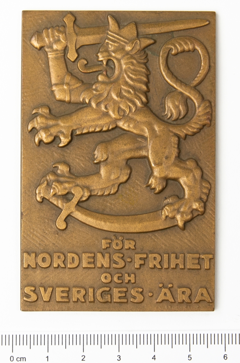 Minnesplakett Svenska Frivilligkåren i Finland. På åtsidan ett präglat motiv av ett lejon och texten "För Nordens Frihet och Sveriges Ära". På frånsidan texten "Svenska Frivilligkåren Krigstjänst i Finland 1940".