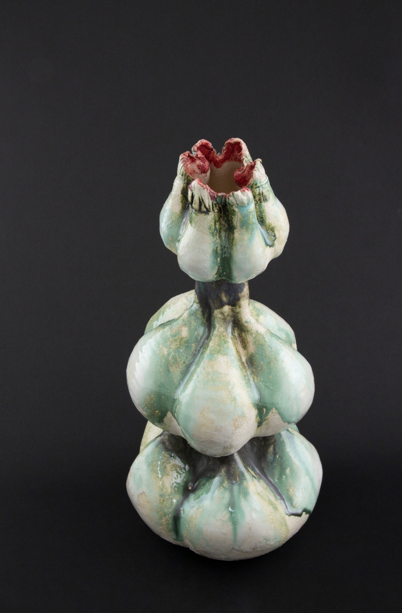 Håndmodellert skulptur i glasert steingods med oppreist holdning. Den har en organisk og asymmetrisk kalebassform som ender i en tulipanform med halvåpne kronblader. Keramikkskulpturen inngår i en installasjon bestående av 26 deler i ulike størrelser og med individuell utforming. De asymmetriske variasjonene gir et inntrykk av bevegelse, og den lett sykelige fargepaletten gir et uhyggelig og grotesk preg. Samtlige deler minner om kjøttetende planter.