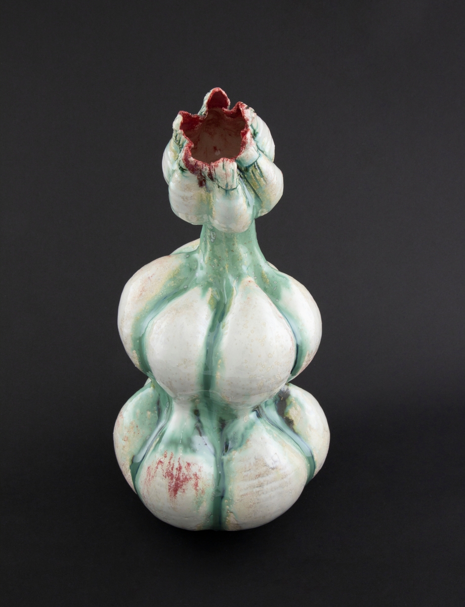 Håndmodellert skulptur i glasert steingods med delvis tiltende hode. Den har en organisk og asymmetrisk kalebassform som ender i en tulipanform med halvåpne kronblader. Keramikkskulpturen inngår i en installasjon bestående av 26 deler i ulike størrelser og med individuell utforming. De asymmetriske variasjonene gir et inntrykk av bevegelse, og den lett sykelige fargepaletten gir et uhyggelig og grotesk preg. Samtlige deler minner om kjøttetende planter.