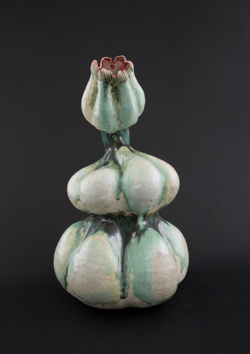 Håndmodellert skulptur i glasert steingods med lett tiltende hode. Den har en organisk og asymmetrisk kalebassform som ender i en tulipanform med halvåpne kronblader. Keramikkskulpturen inngår i en installasjon bestående av 26 deler i ulike størrelser og med individuell utforming. De asymmetriske variasjonene gir et inntrykk av bevegelse, og den lett sykelige fargepaletten gir et uhyggelig og grotesk preg. Samtlige deler minner om kjøttetende planter.