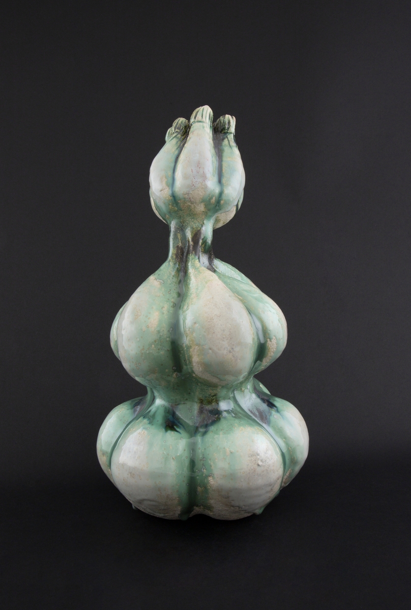 Håndmodellert skulptur i glasert steingods med oppreist holdning og litt tiltet hode. Den har en organisk og asymmetrisk kalebassform som ender i en tulipanform med halvåpne kronblader. Keramikkskulpturen inngår i en installasjon bestående av 26 deler i ulike størrelser og med individuell utforming. De asymmetriske variasjonene gir et inntrykk av bevegelse, og den lett sykelige fargepaletten gir et uhyggelig og grotesk preg. Samtlige deler minner om kjøttetende planter.