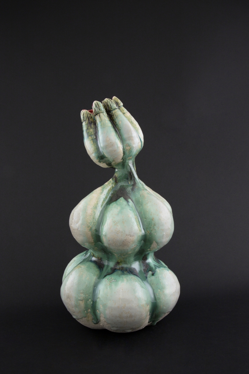 Håndmodellert skulptur i glasert steingods med oppreist holdning og litt tiltet hode. Den har en organisk og asymmetrisk kalebassform som ender i en tulipanform med halvåpne kronblader. Keramikkskulpturen inngår i en installasjon bestående av 26 deler i ulike størrelser og med individuell utforming. De asymmetriske variasjonene gir et inntrykk av bevegelse, og den lett sykelige fargepaletten gir et uhyggelig og grotesk preg. Samtlige deler minner om kjøttetende planter.