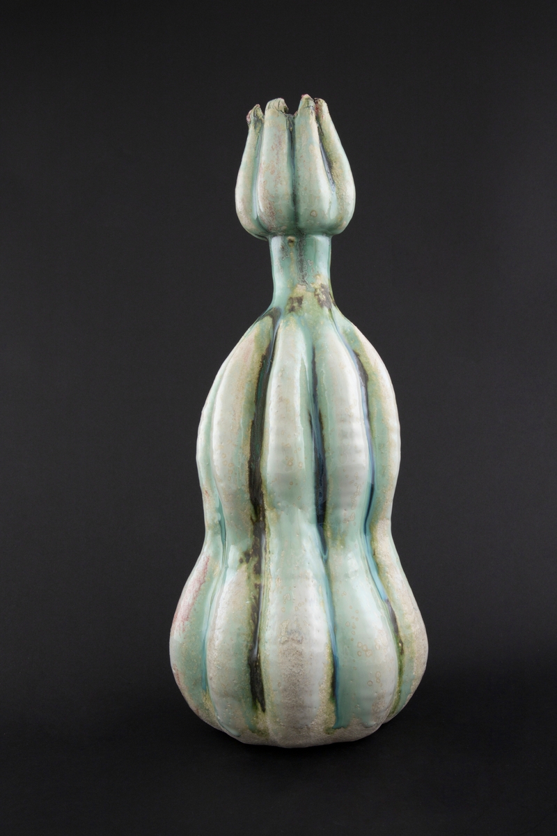 Håndmodellert skulptur i glasert steingods med oppreist holdning. Den har en organisk og asymmetrisk kalebassform som ender i en tulipanform med halvåpne kronblader. Keramikkskulpturen inngår i en installasjon bestående av 26 deler i ulike størrelser og med individuell utforming. De asymmetriske variasjonene gir et inntrykk av bevegelse, og den lett sykelige fargepaletten gir et uhyggelig og grotesk preg. Samtlige deler minner om kjøttetende planter.